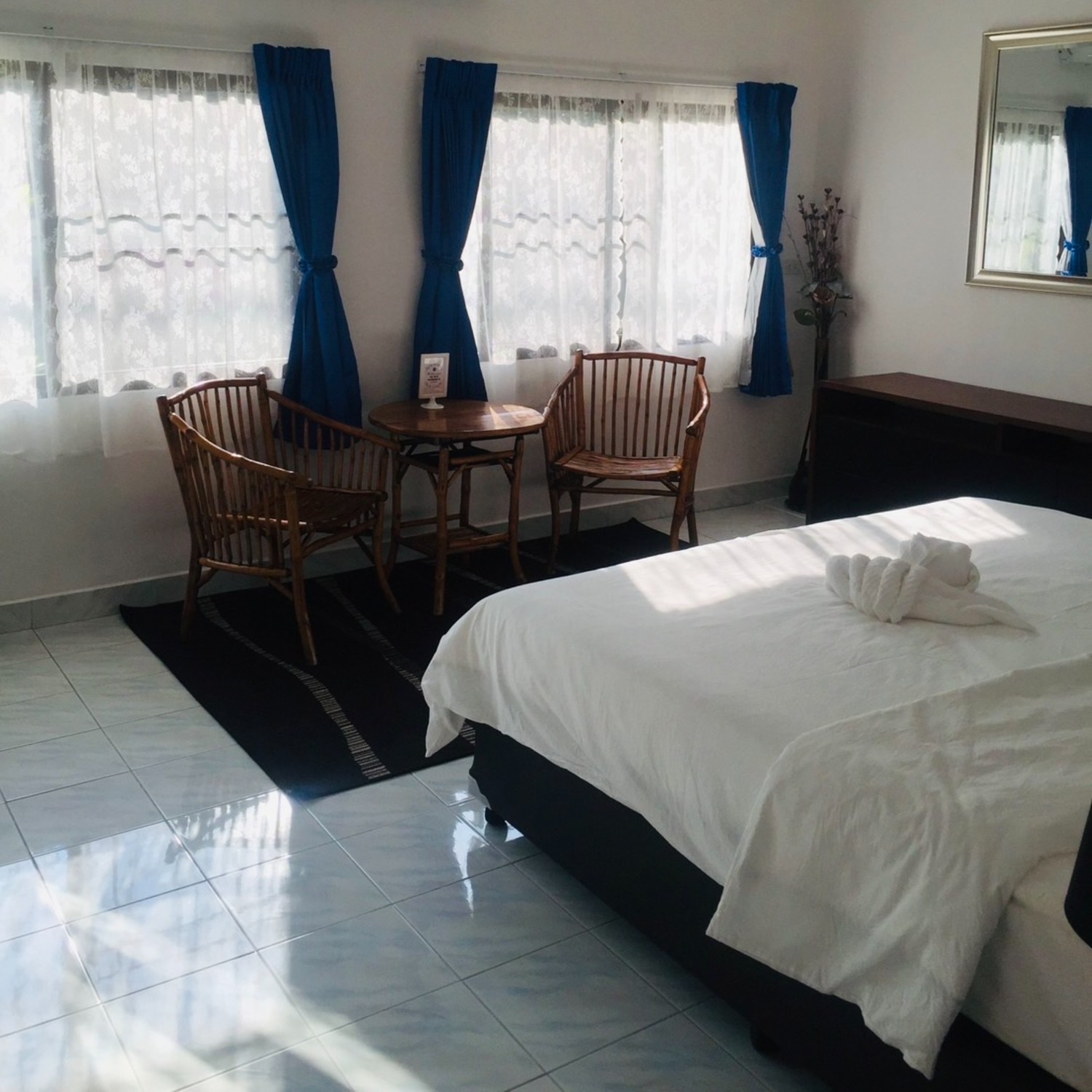 The spacious Deluxe Double Room at Lyndale Lodge with a large bed, bright windows and blue curtains